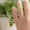 Hand wearing 14K yellow gold birthstone stackable rings with 2mm round stones sizes 4-10 on a white fabric with green plant in background  
